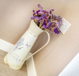 A metal pitcher with dried purple flowers on the floor against a beige wall with a white electrical outlet at Lavender Lodge in Charlton Horethorne near Sherborne