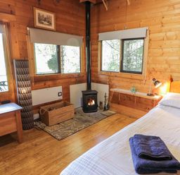 A bedroom with a bed fire stove wicker basket and wooden furniture at The Log Cabin in Oban