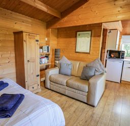 A room with a bed with towels a beige sofa a wooden wardrobe and a kitchen area at The Log Cabin in Oban