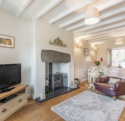A living room with a television on a stand a wood burning stove a brown leather armchair and a dining table with chairs at 2 Bryn Tirion in Llan Ffestiniog