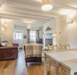 A living room and dining area with wooden floor a dining table with chairs and flowers on the table at 2 Bryn Tirion in Llan Ffestiniog
