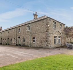 A stone building with multiple windows and outdoor chairs and table on the side at Reiver's Rest in Hesleyside near Bellingham