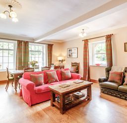 A living room with a red sofa and a wooden coffee table next to a black sofa with plaid cushions at Reiver's Rest in Hesleyside near Bellingham