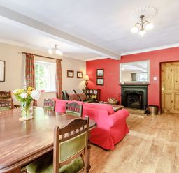 A living room with a wooden dining table and chairs red sofas a fireplace and a television at Reiver's Rest in Hesleyside near Bellingham