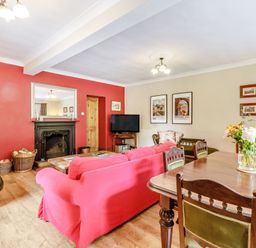 A living room with red walls a fireplace a red sofa wooden dining table and flower vase at Reiver's Rest in Hesleyside near Bellingham