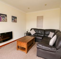 A living room with a brown leather sectional sofa wooden coffee table and wall-mounted electric fireplace at Glen Dessary in Corpach near Fort William