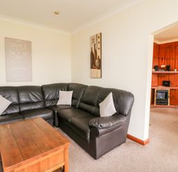 A living room with a brown leather corner sofa a wooden coffee table and wall art at Glen Dessary in Corpach near Fort William