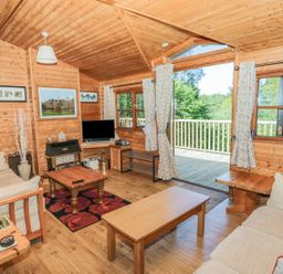 A wooden living room with sofas coffee tables a television and an open door leading to a deck at Striding Edge White Cross Bay near Troutbeck Bridge