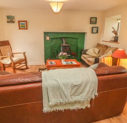 A living room with a brown leather sofa and light green throw blanket facing a green fireplace wooden rocking chair and small sofa with cushions at Nanas House in Allihies County Cork