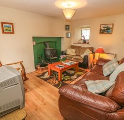 A living room with a wood stove a coffee table two sofas a wooden chair and a television at Nanas House in Allihies County Cork