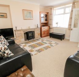 A living room with two black leather sofas a rug a wooden cabinet and a fireplace at Lyndhurst Cottage in Beadnell