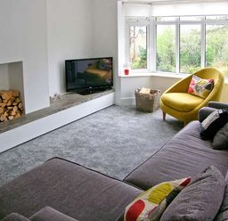 A living room with a grey sofa and a yellow armchair near a bay window with a television and a fireplace with firewood at Llechwedd in Dolgellau