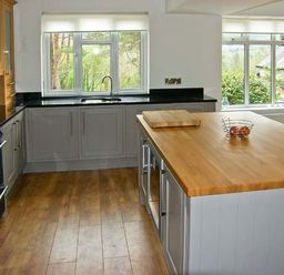A kitchen with wooden flooring a central island with a wooden countertop and cabinets under windows at Llechwedd in Dolgellau