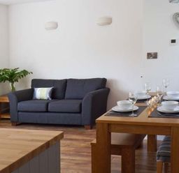 A living room with a dark grey sofa a wooden dining table set with white bowls and glasses and a wooden side table with a plant at Llechwedd in Dolgellau