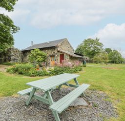 A picnic table on a gravel area in a garden with a stone cottage and flowers at The Shippon in Llechwedd The Conwy Valley