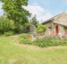 A stone cottage with a red door surrounded by grass trees and a flower garden at The Shippon in Llechwedd The Conwy Valley