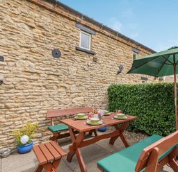 An outdoor patio with wooden benches and table set with plates and drinks next to a stone wall and green umbrella at Upstairs Downstairs Cottage in Snainton near Scarborough