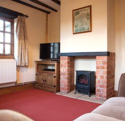 A living room with a fireplace a television on a wooden cabinet and a window with curtains at Yew Tree Cottage in Little Malvern near Malvern