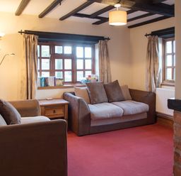 A living room with two sofas a wooden side table books on windowsill and curtains at Yew Tree Cottage in Little Malvern near Malvern