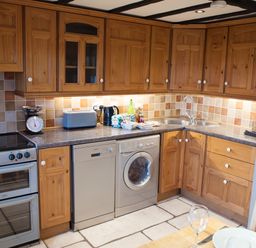 A kitchen with wooden cabinets a stove dishwasher washing machine and a sink at Yew Tree Cottage in Little Malvern near Malvern