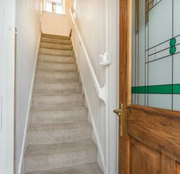 A carpeted staircase with white walls and a wooden door with patterned glass at Hillside Cottage in Peasedown St John near Bath