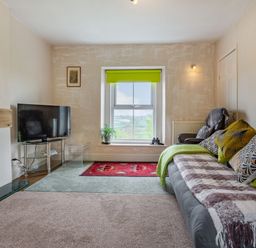 A living room with a sofa pillows a television on a glass stand and a window with a green blind at Hillside Cottage in Peasedown St John near Bath
