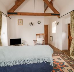 A living room with wooden beams a rocking chair and a television at High Park Barn in Uffculme Blackdown Hills