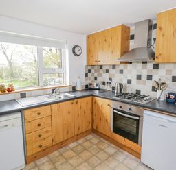 A kitchen with wooden cabinets, a gas stove, oven, dishwasher, fridge, sink, and a window at Mary Kates Cottage in Narin County Donegal