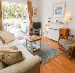 A living room with a sofa pillows coffee table armchair television and open doors to a deck at Waterside Cottage in Little Petherick Creek near Padstow