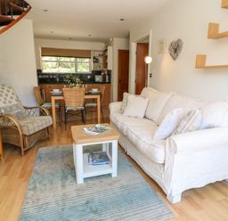 A living room with a white sofa a small table and an armchair next to a dining table with chairs and a kitchen in the background at Waterside Cottage in Little Petherick Creek near Padstow