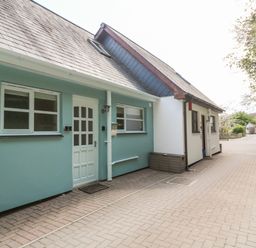 Exterior view of a row of houses with paved driveway and trees on the right at Waterside Cottage in Little Petherick Creek near Padstow
