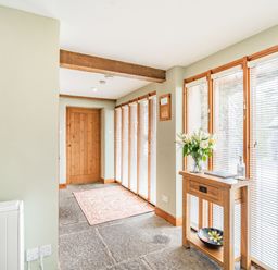 A hallway with stone floor wooden door console table with flowers and a bowl and windows with blinds at Moresdale Bank Cottage Lambrigg near Sedbergh and Kendal