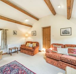 A living room with wooden ceiling beams two patterned sofas an armchair a small wooden table a floor lamp and framed pictures at Moresdale Bank Cottage Lambrigg near Sedbergh and Kendal
