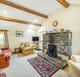 A living room with a stone fireplace wooden beams armchairs a sofa and a rug at Moresdale Bank Cottage Lambrigg near Sedbergh and Kendal