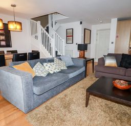 A living room with two sofas pillows a coffee table and a dining area with chairs and pendant lights at Lodge 22 Cherry in Wadebridge