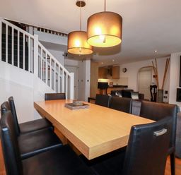 A dining area with a wooden table and black chairs near a staircase and a living room with a sofa at Lodge 22 Cherry Wadebridge