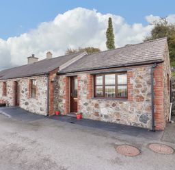 Stone cottage with multiple windows and a door on a paved driveway at Penrallt Cottage in Y Felinheli near Caernarfon