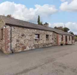 A stone cottage with small windows and flower pots outside on a paved area at Penrallt Cottage in Y Felinheli near Caernarfon
