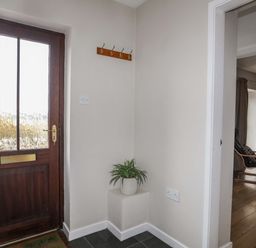 An entryway with a wooden door a potted plant on a small pedestal and a wooden coat rack at Penrallt Cottage in Y Felinheli near Caernarfon