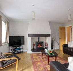 A living room with a fireplace television armchairs and a sofa at Penrallt Cottage in Y Felinheli near Caernarfon