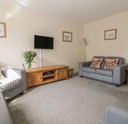 A sitting room with gray sofas a wooden coffee table a flat screen TV and framed pictures on walls at Sandlings Hollesley near Woodbridge