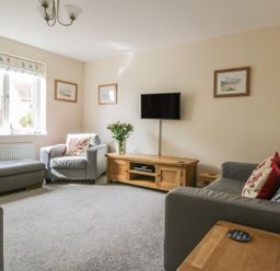 A living room with grey sofas a wooden TV stand with a flat screen TV and framed pictures on the wall at Sandlings Hollesley near Woodbridge