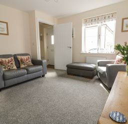 A living room with two gray sofas a gray ottoman a wooden table with flowers and two framed pictures on the wall at Sandlings Hollesley near Woodbridge