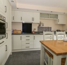 A kitchen with white cabinets a wooden dining table and chairs at Sandlings in Hollesley near Woodbridge