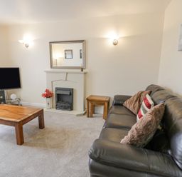 A living room with a leather sofa a wooden coffee table a TV on a stand and a fireplace at Gwelfor in Morfa Bychan