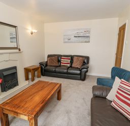 A living room with leather sofas wooden tables and a fireplace at Gwelfor in Morfa Bychan