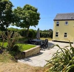 A garden with outdoor dining table and chairs, trees, grass, and a yellow house at Gwelfor in Morfa Bychan
