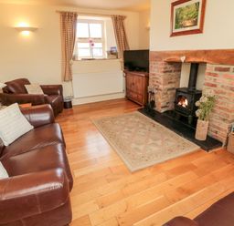 A living room with leather sofas a brick fireplace with a wood stove a rug and wooden floor at The Granary in Longframlington near Alnwick
