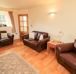 A living room with three brown leather sofas a wooden floor a rug and a wooden door at The Granary in Longframlington near Alnwick