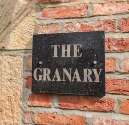 A black stone plaque with the words The Granary on a brick and stone wall at The Granary in Longframlington near Alnwick